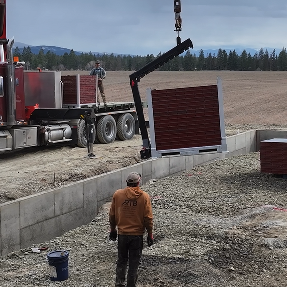 A man is standing in front of a truck that has a crane attached to it. Project done by Raise the Bar Construction