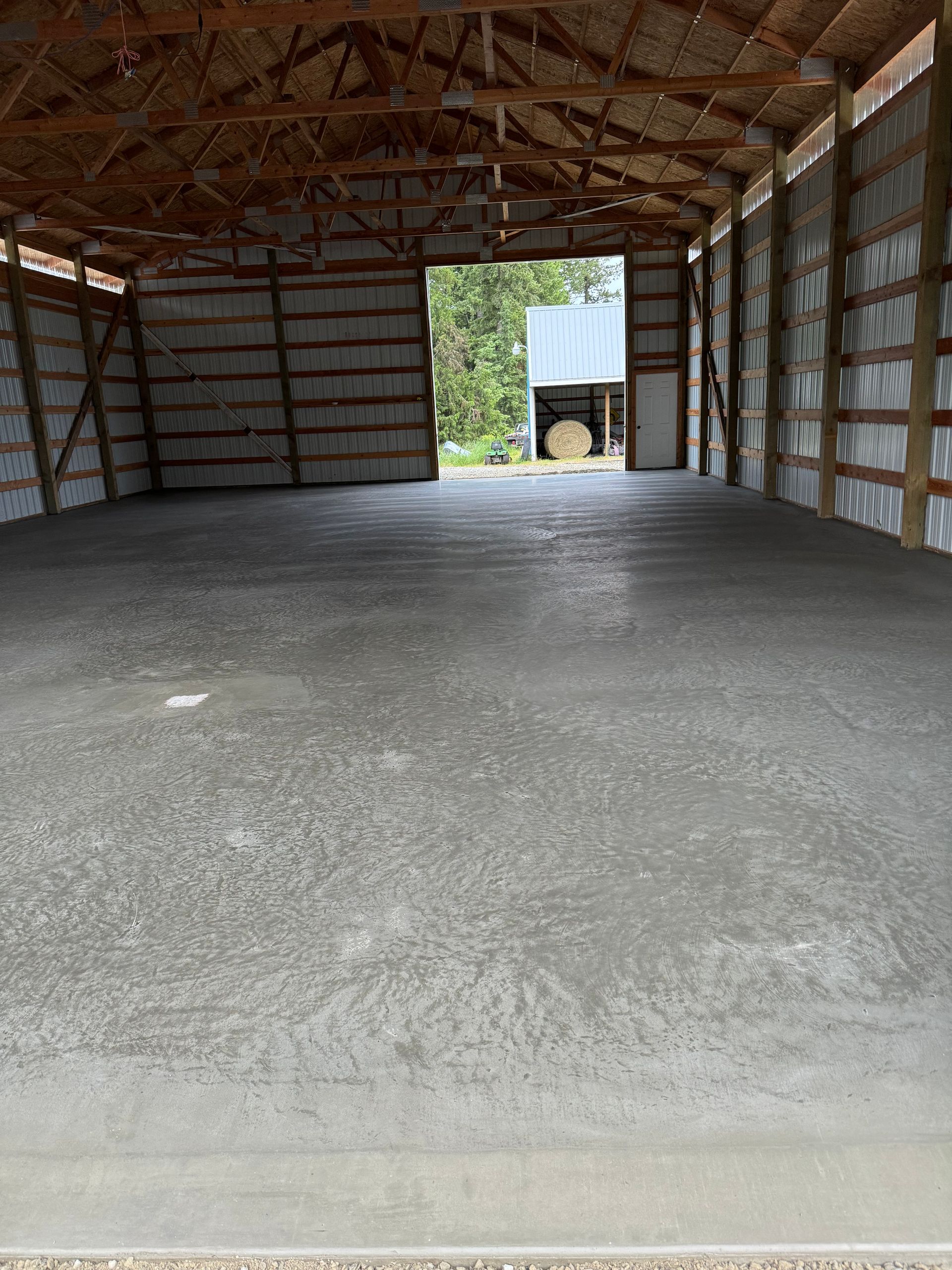 The inside of a barn with a concrete floor and a wooden roof. Project done by Raise the Bar Construction