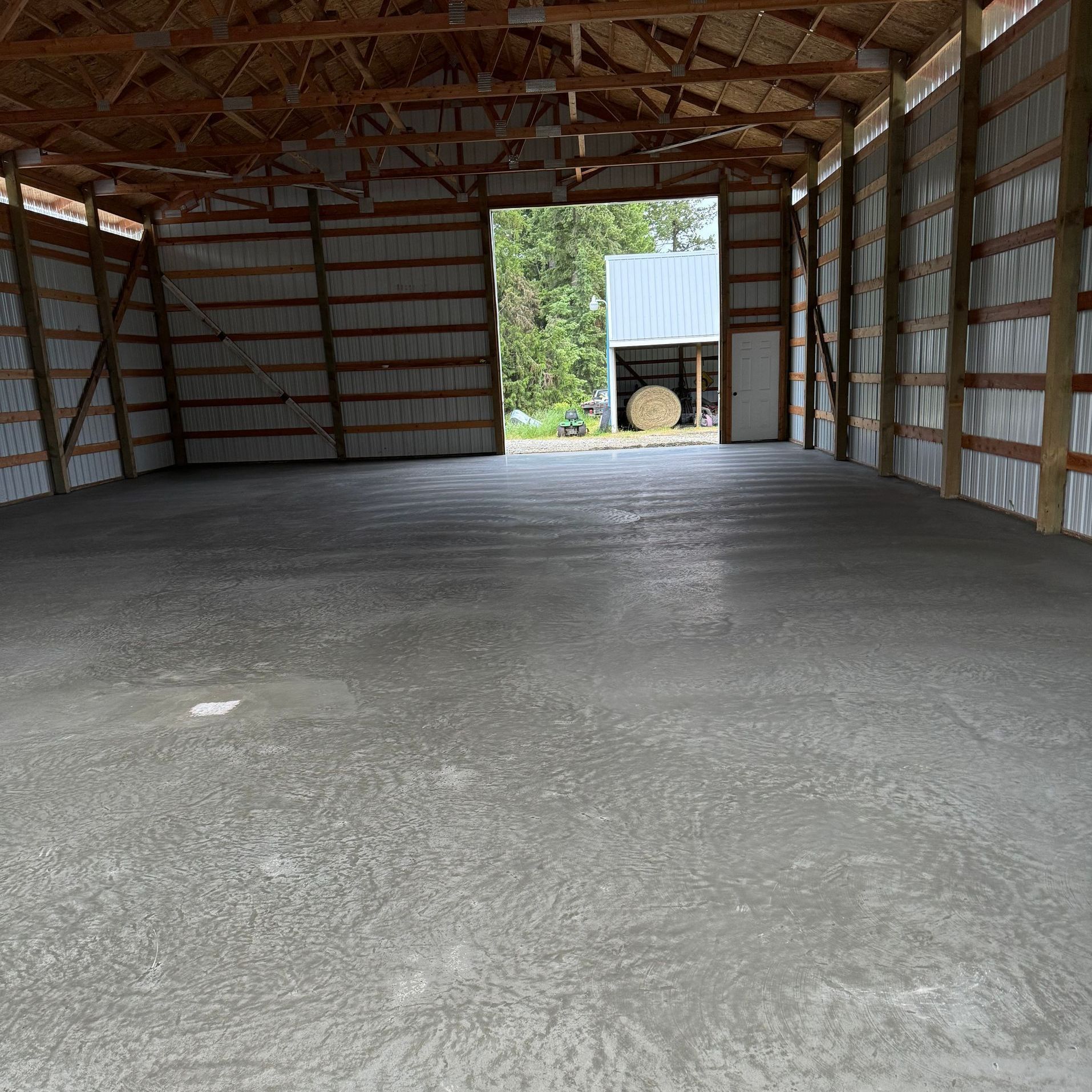 An empty barn with a concrete floor and a wooden roof. Project done by Raise the Bar Construction