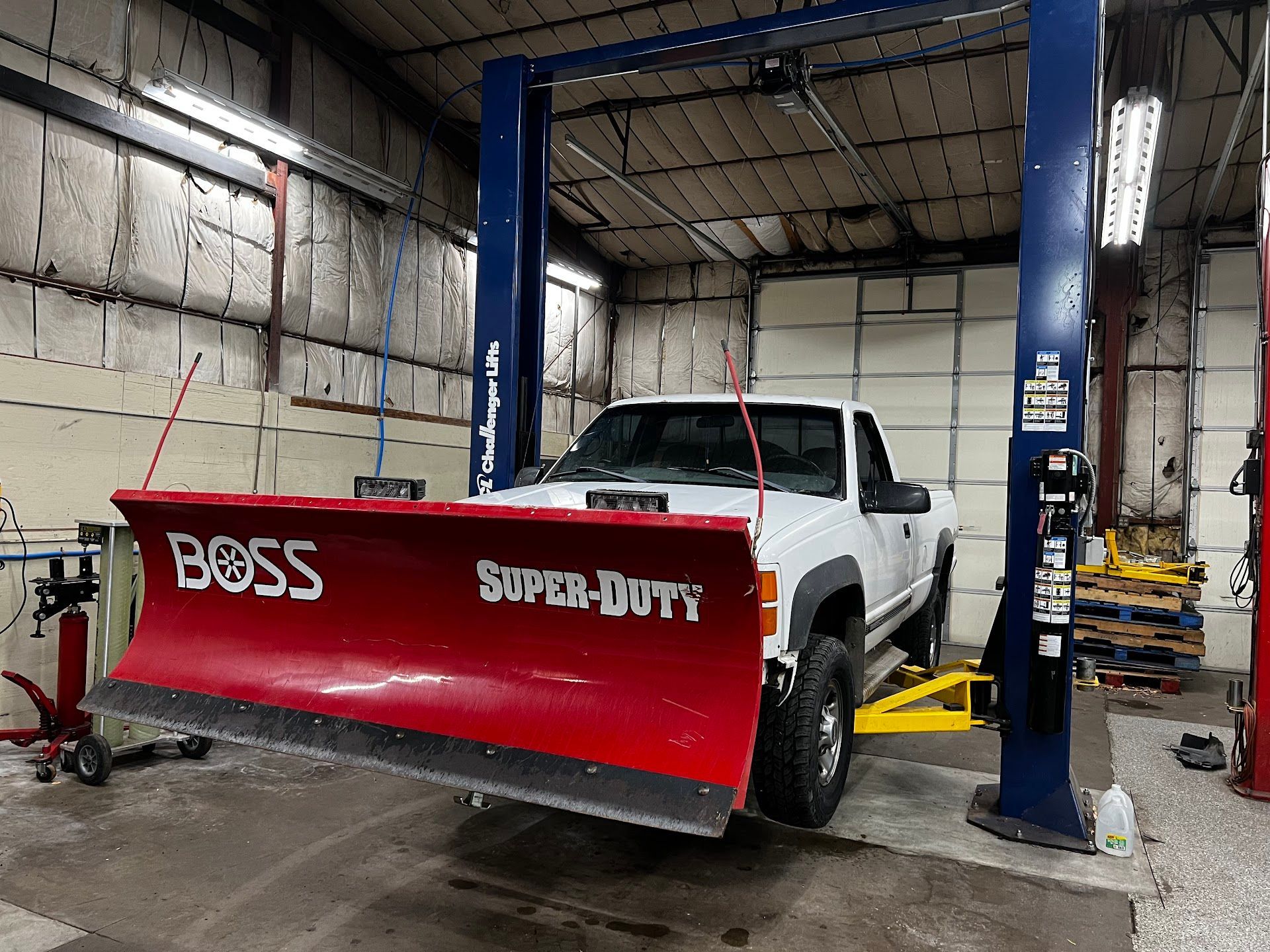 White truck with red Boss Super-Duty snowplow raised on a lift inside a garage | 6 to 6 Auto Service
