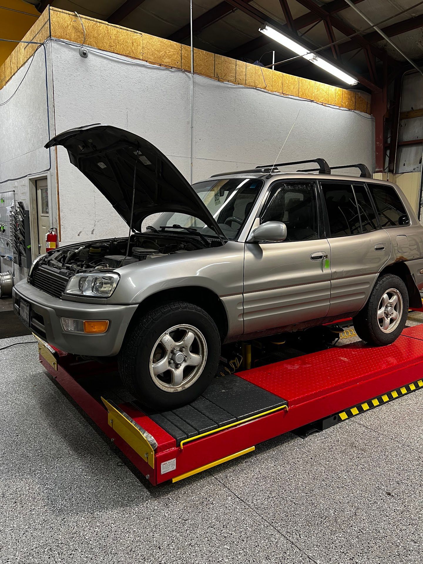 Silver SUV with hood open on a red car lift in a garage | 6 to 6 Auto Service