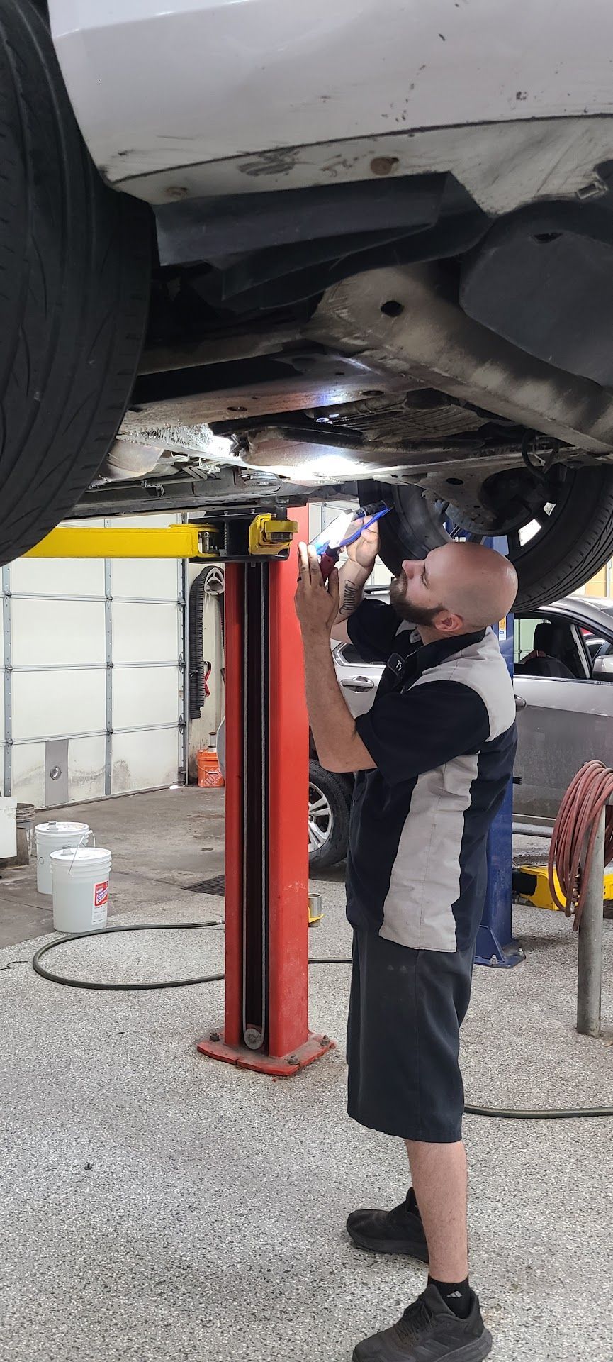 Mechanic working under a car lifted on a red hoist in a garage | 6 to 6 Auto Service