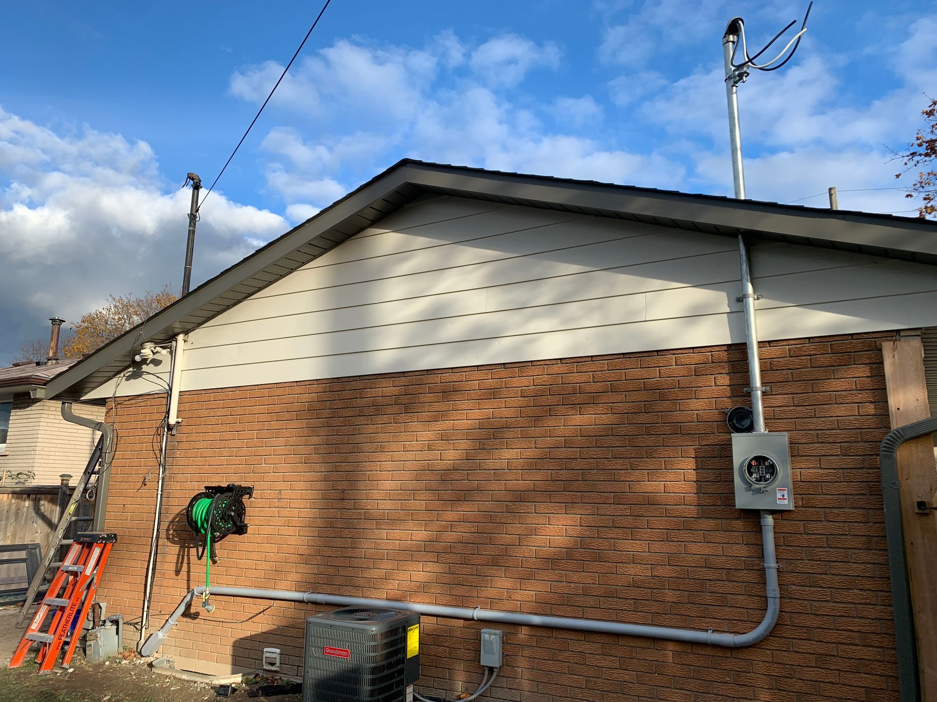 A brick house with a ladder and a fan on the side of it.
