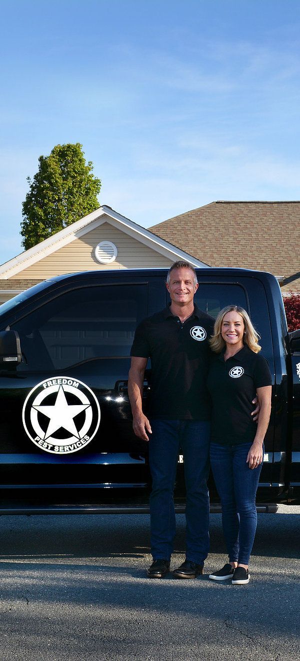Two people stand next to a black truck. They wear black shirts and blue jeans, smiling in front of a house.