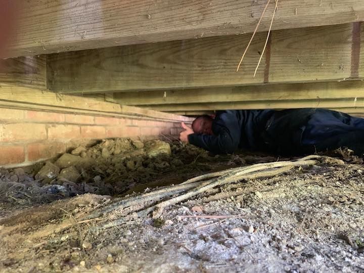Person examining crawl space under wooden beams and brick foundation.