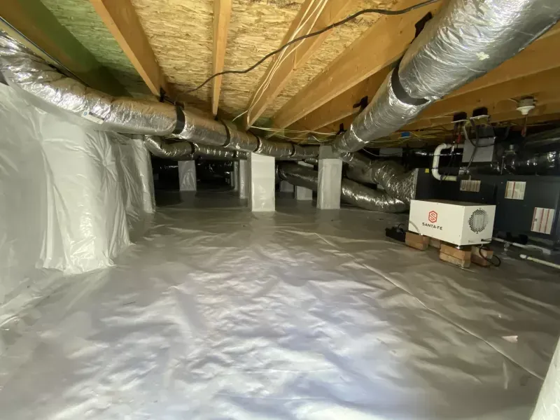 Crawl space with white vapor barrier flooring and walls, wooden beams, HVAC ductwork, and support columns.