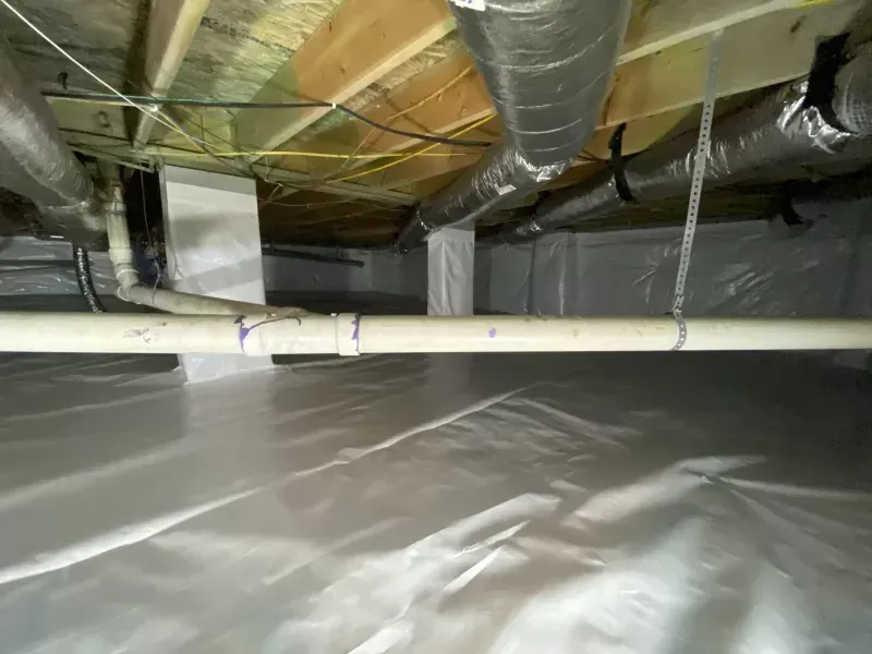 Crawl space with white plastic sheeting, pipes, ductwork, and wooden beams.