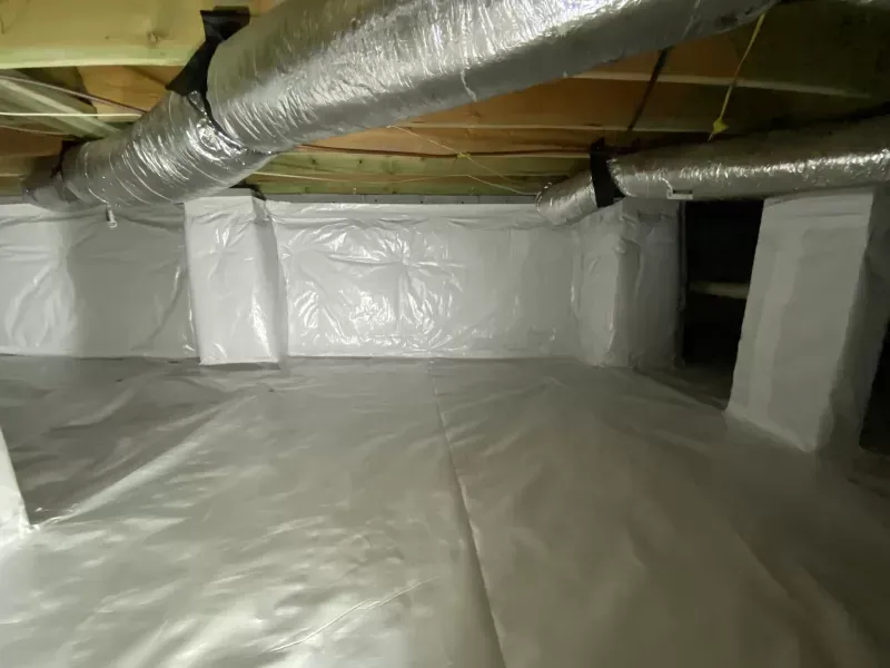 Crawl space with white plastic vapor barrier on the floor and walls, silver ductwork, and support beams.