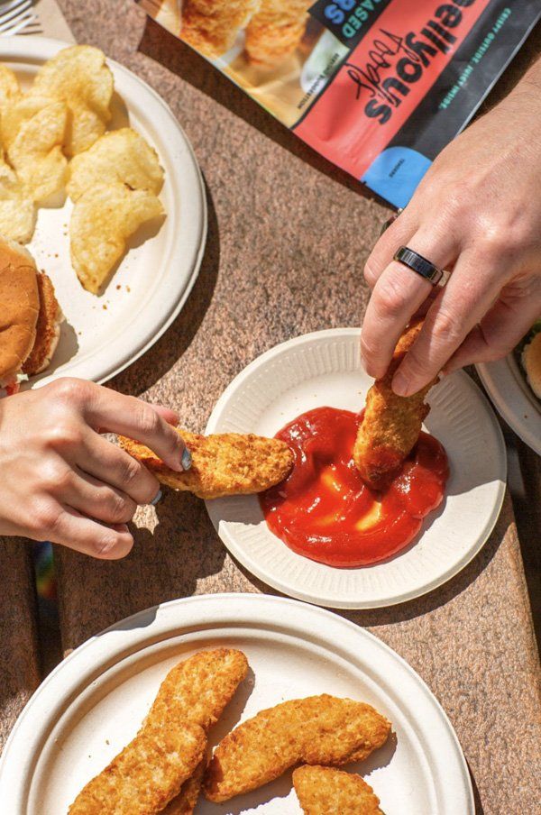 hands dunking chicken tenders in ketchup