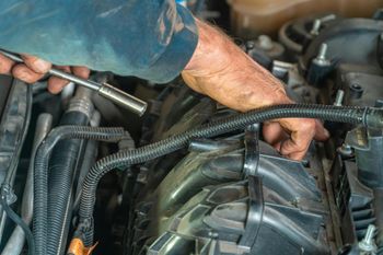 Mechanic’s hands working in a car engine bay, tightening a component with a wrench | Geiger’s Automotive & Diesel Repair