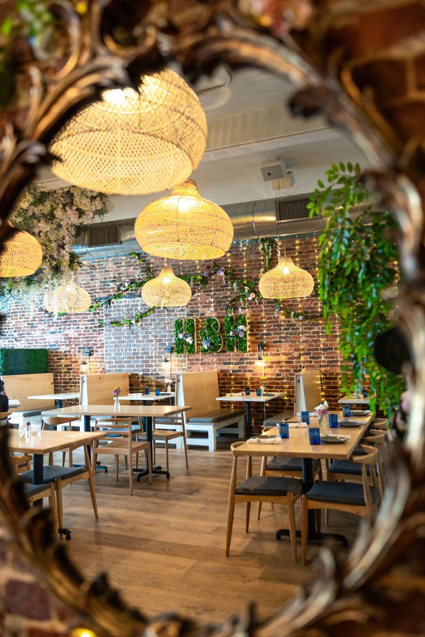 Mirror reflecting a restaurant interior with tables, pendant lights, and brick wall.