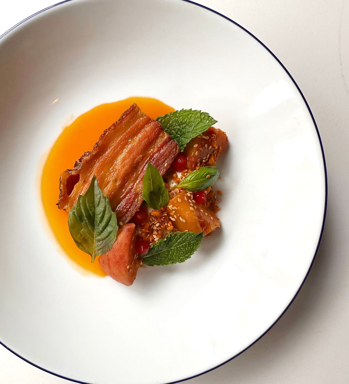 Belly pork dish in a white bowl with orange sauce, mint garnish, and what appears to be a crumb topping.