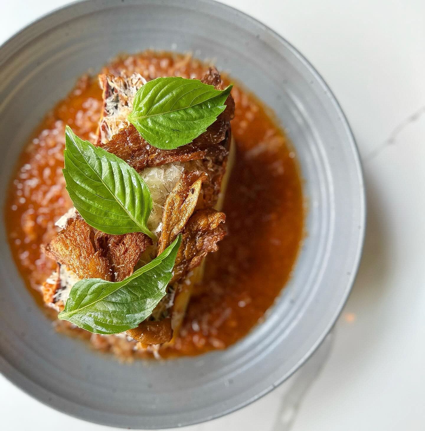 Lasagna in tomato sauce, garnished with fresh basil leaves, in a gray bowl.