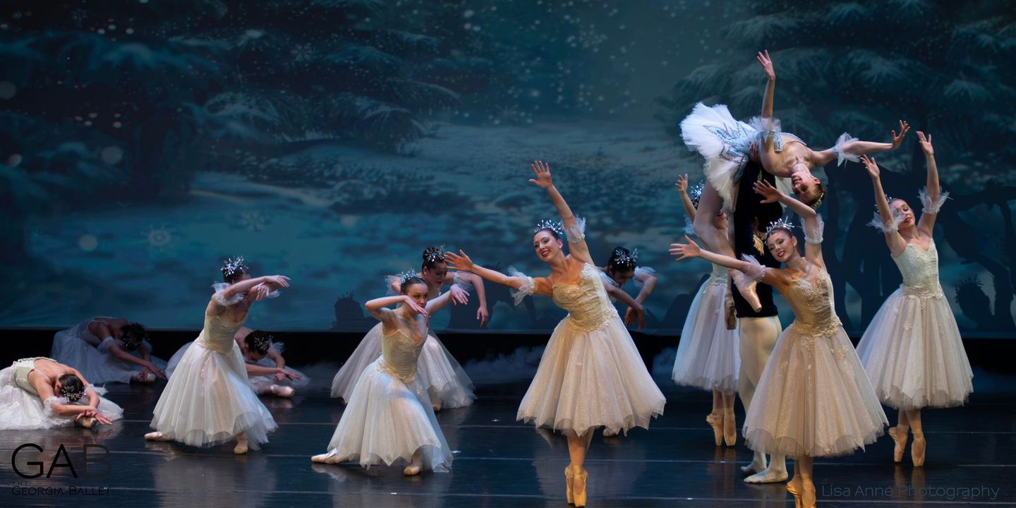 Two ballet dancers, in a theatrical setting, touch hands over the logo