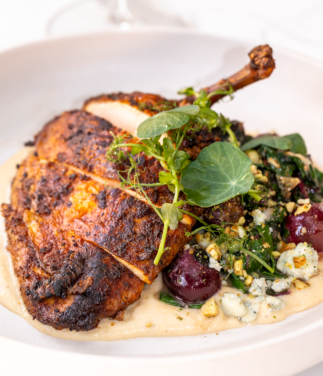 Roasted chicken breast with leg, served with greens, sauce, and garnishes.