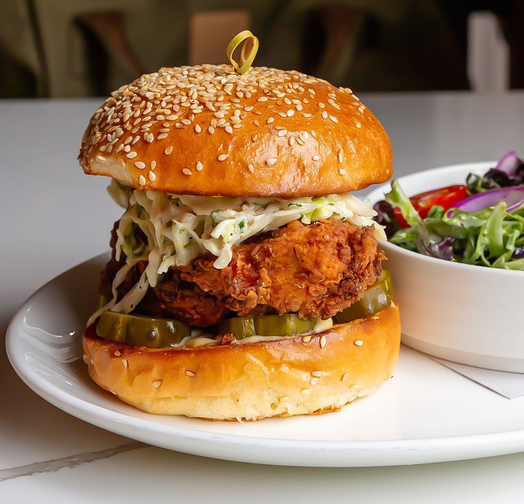 Crispy fried chicken sandwich with coleslaw, pickles, and sesame seed bun, served with salad.
