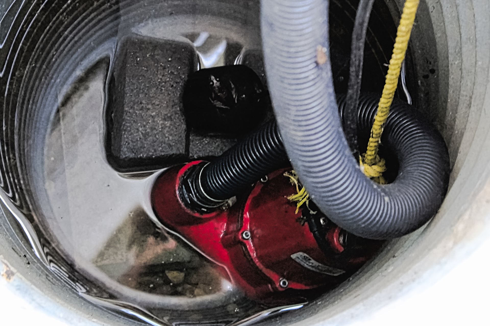 A red pump is sitting in a hole with a hose attached to it