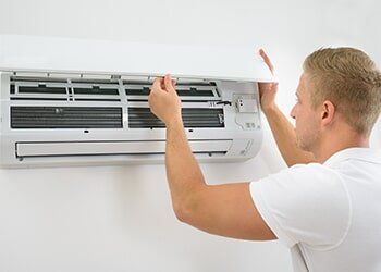 Heating Repair — Man Fixing an Air Conditioning Unit in Dallas, TX