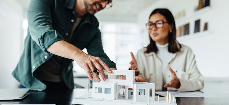 a man with his hand on a model of a building with a woman looking on