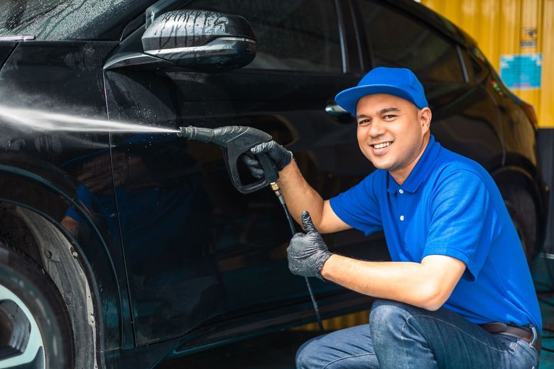 Man smiling with thumb up while spraying car with water