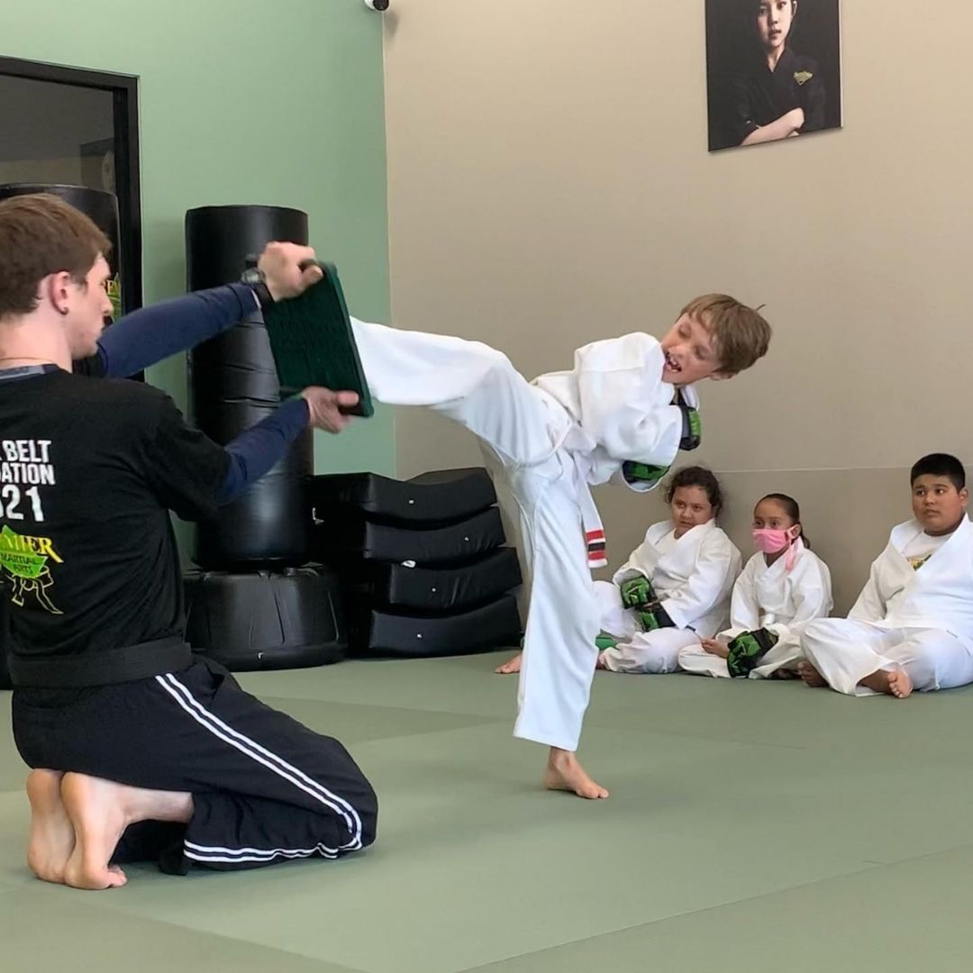 A young girl in a karate uniform is sitting on the floor.