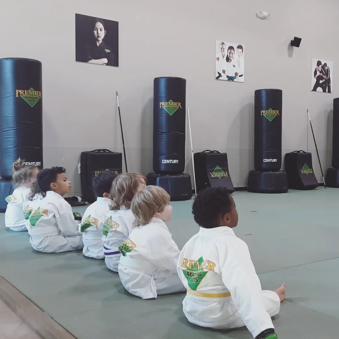 A group of children are practicing karate with a teacher in a gym.