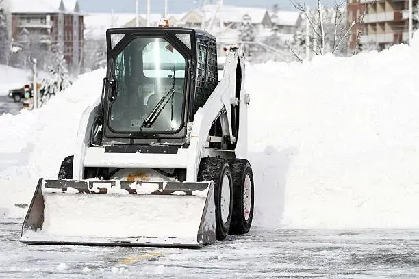 Snow-covered skid-steer loader clearing a path in a snowy urban area