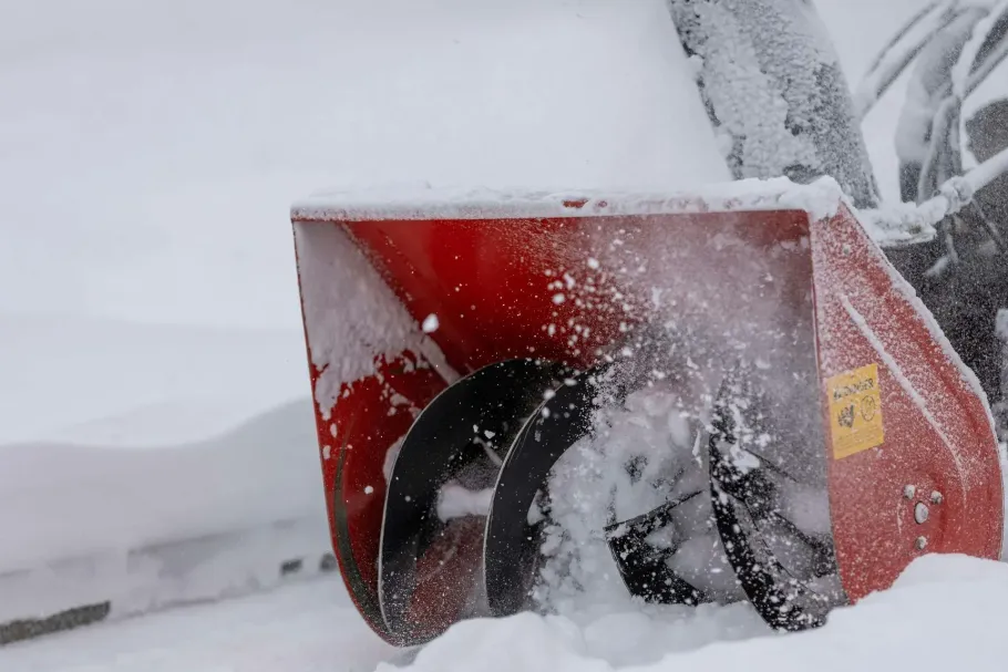 Red snowblower clearing snow, with snow packed around its chute and blade.