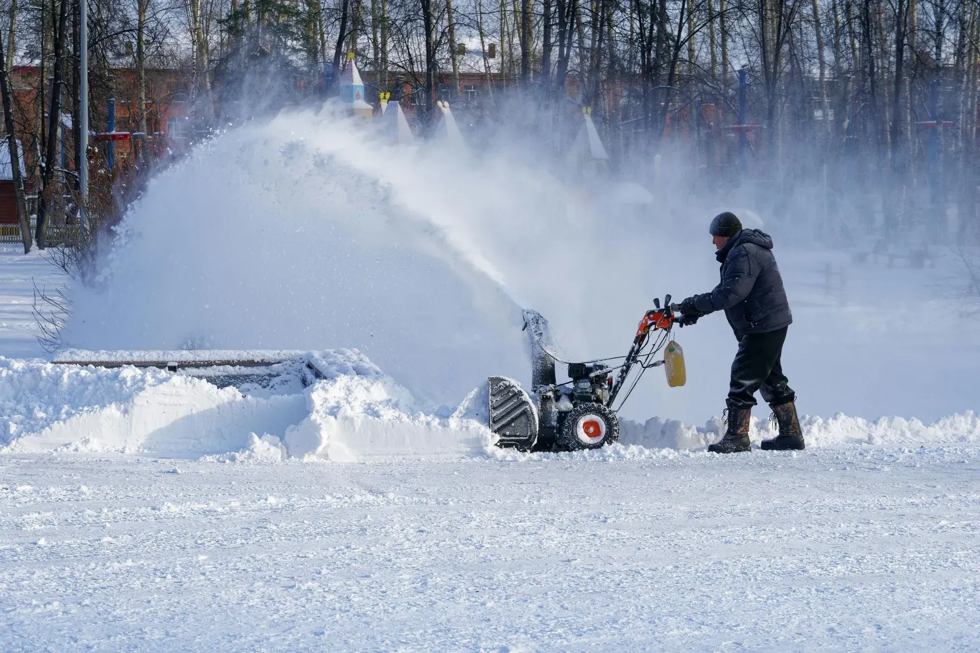 Person operating a snow blower on a snowy field, spraying snow into the air.