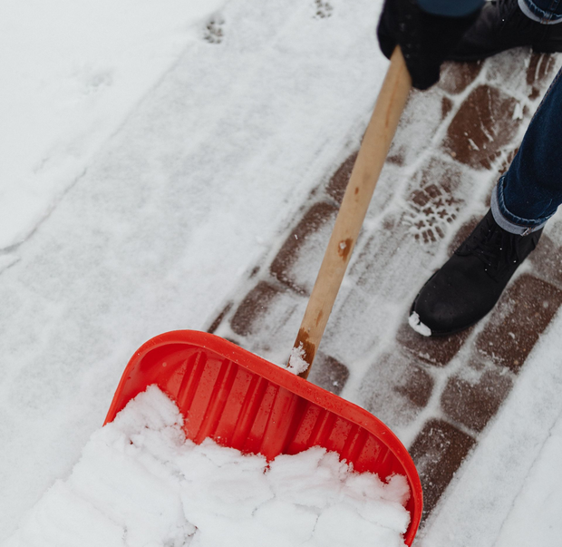 Person shoveling snow with a red shovel on a brick walkway
