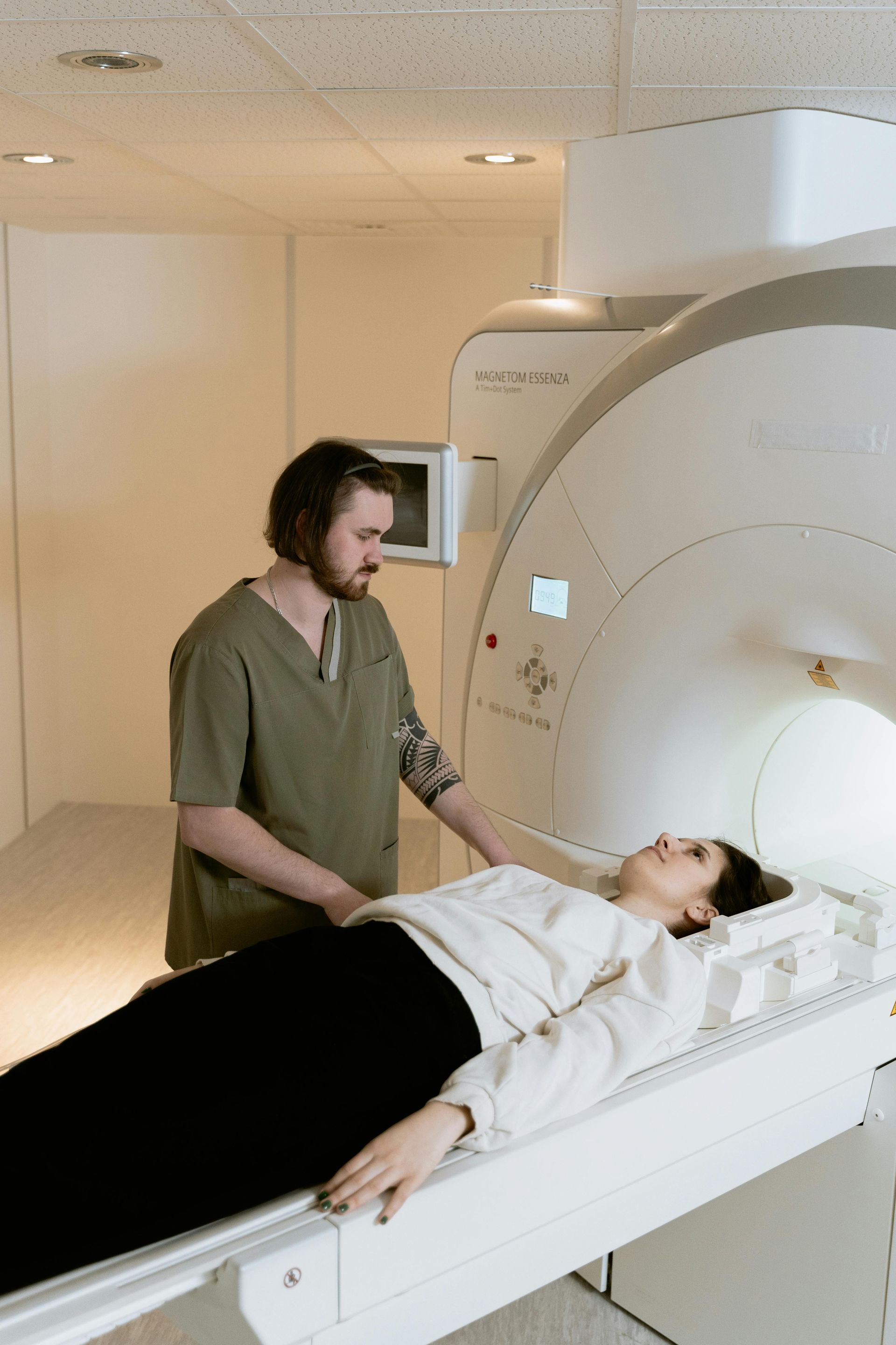 A man is standing next to a woman laying on a bed in front of a mri machine.