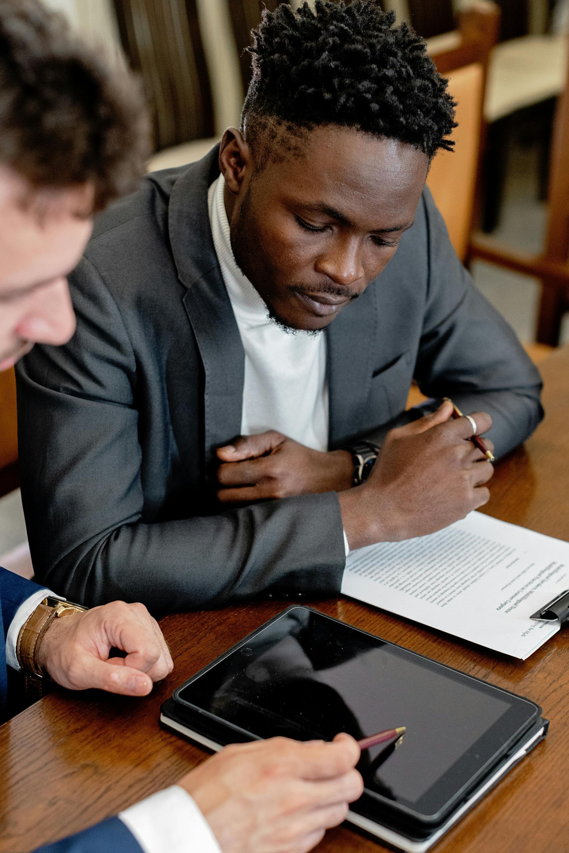 Two men are sitting at a table looking at a tablet.