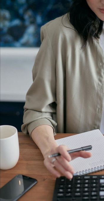 A woman is sitting at a table using a calculator and a pen.