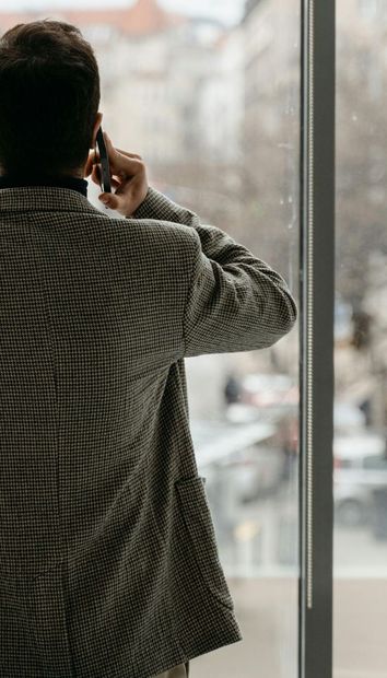 A man is standing in front of a window talking on a cell phone.