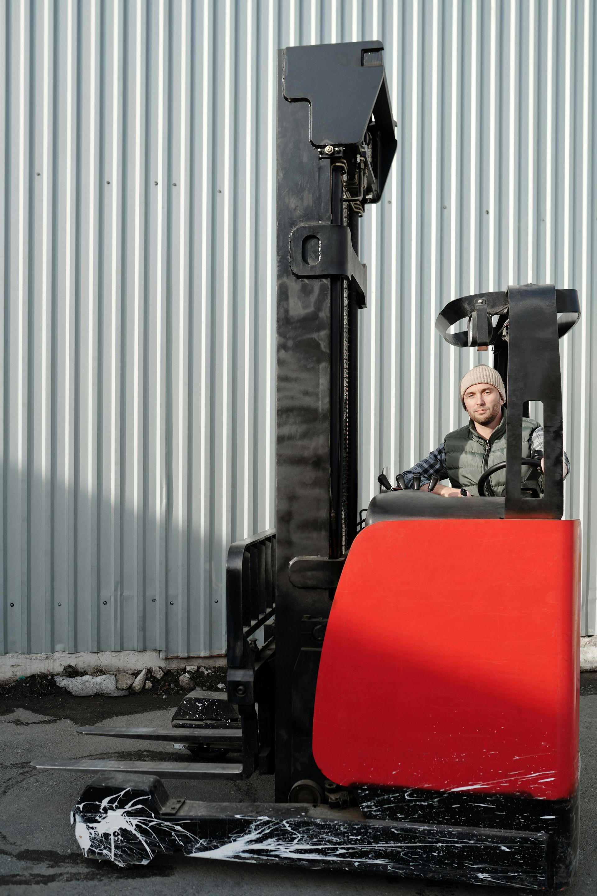 A man is driving a red forklift in front of a building.