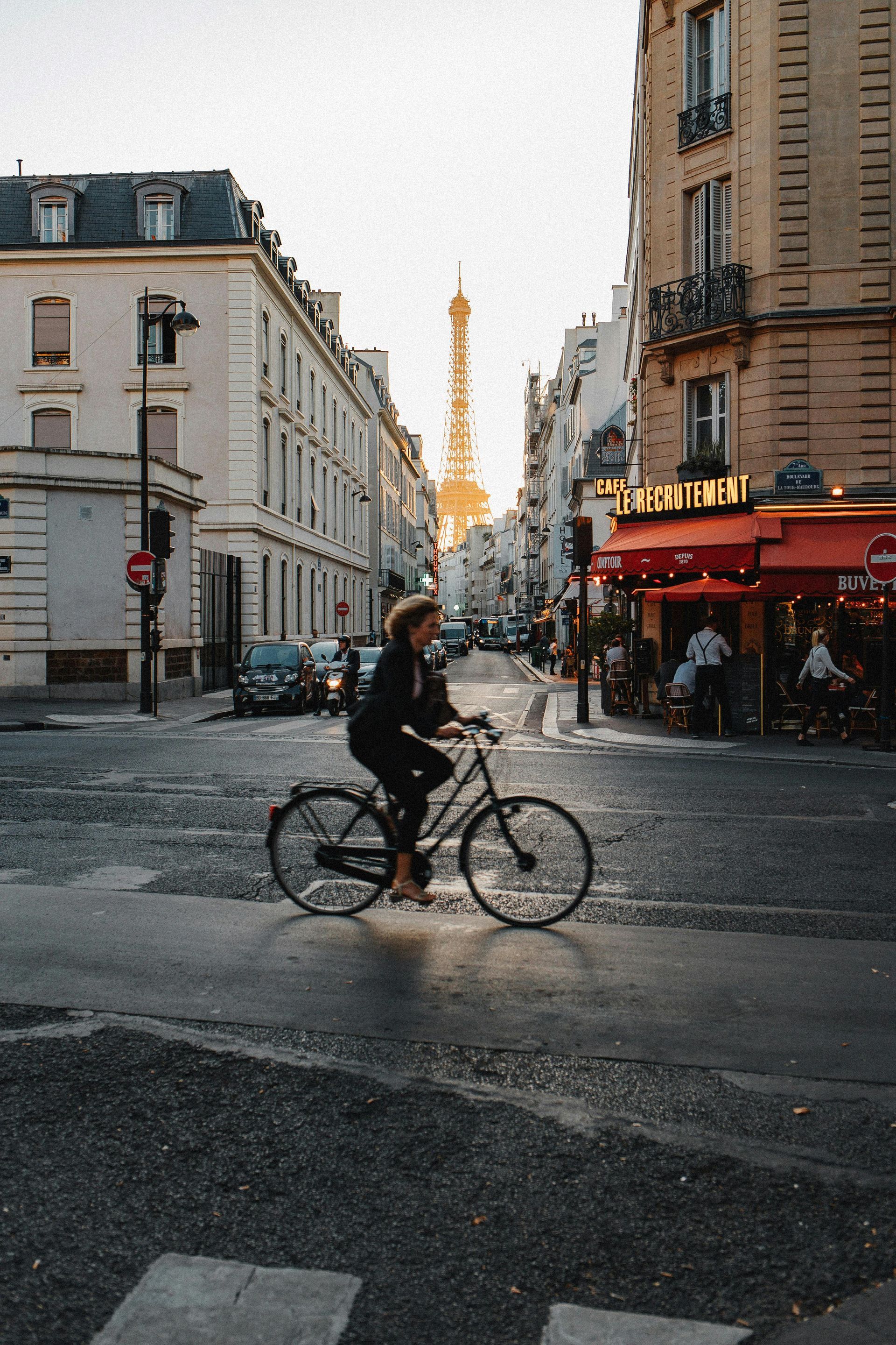 A woman is riding a bike down a city street with the eiffel tower in the background.