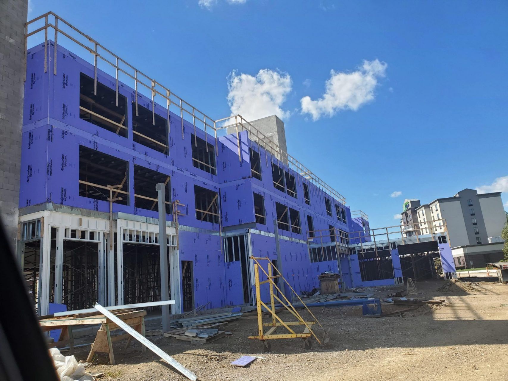 A large building is being built with large steel panels being construction with  purple insulation panels.