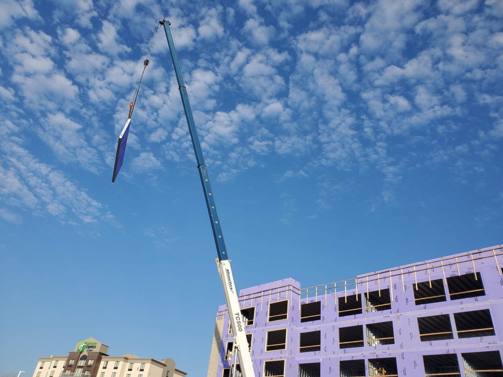 A crane is lifting a flag in front of a building under construction.