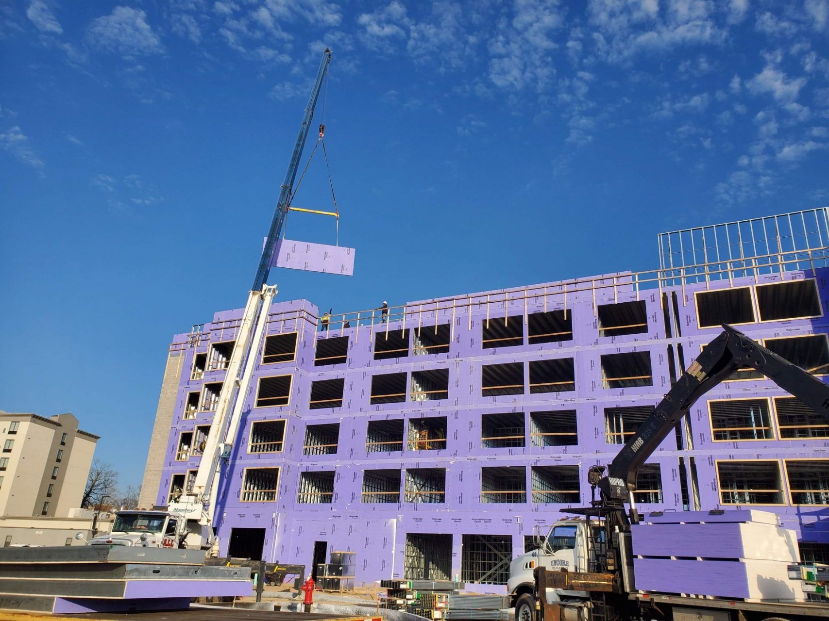A crane is lifting a large steel section of in front of a building under construction.