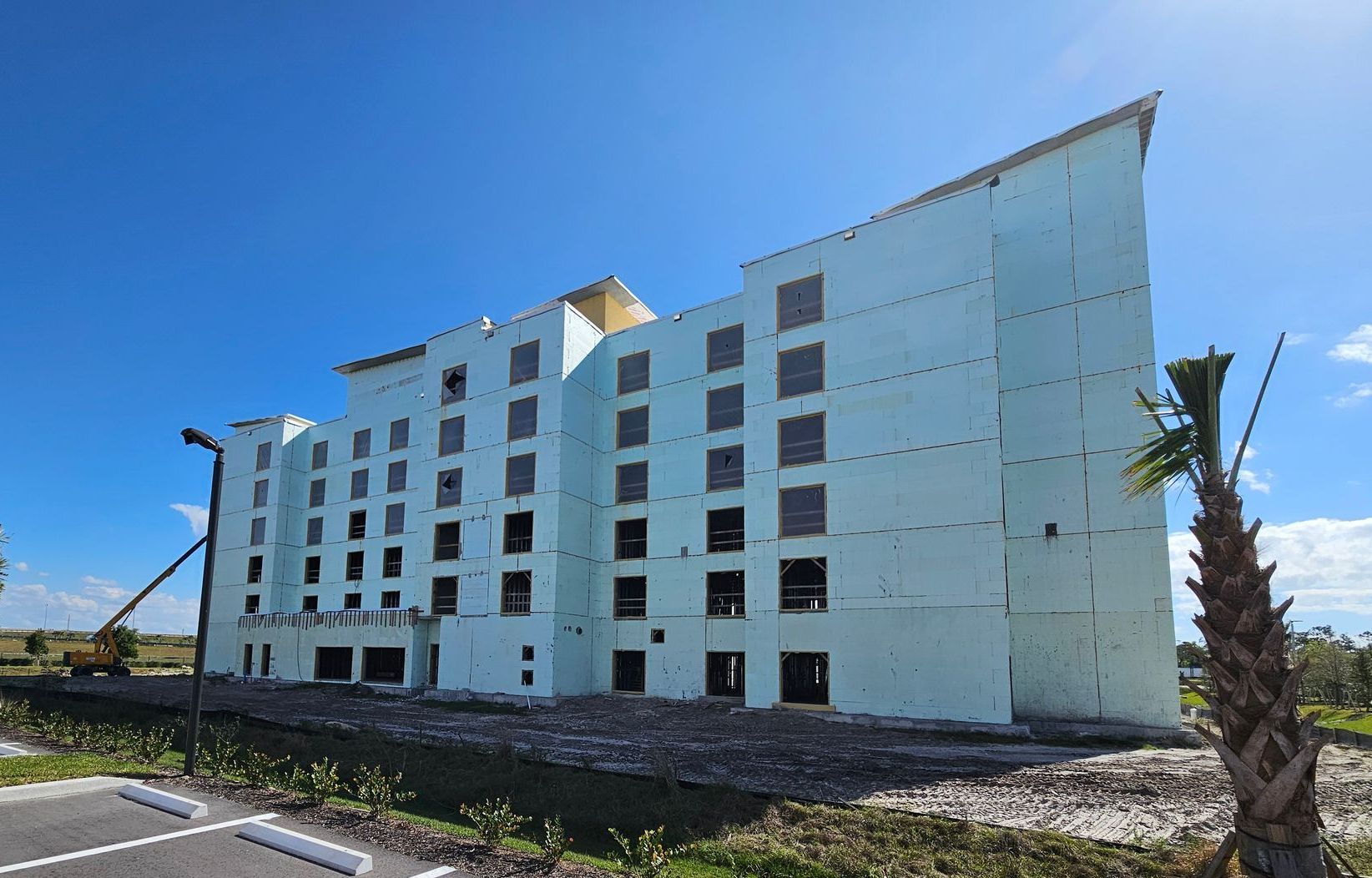 A large white building under construction with a palm tree in front of it.