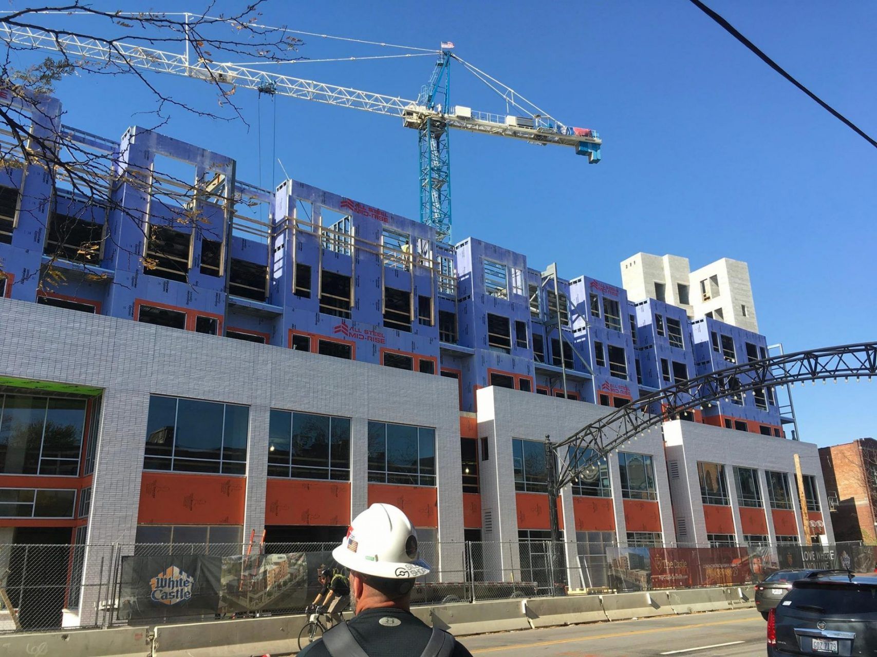 A man wearing a hard hat is standing in front of a building under construction.