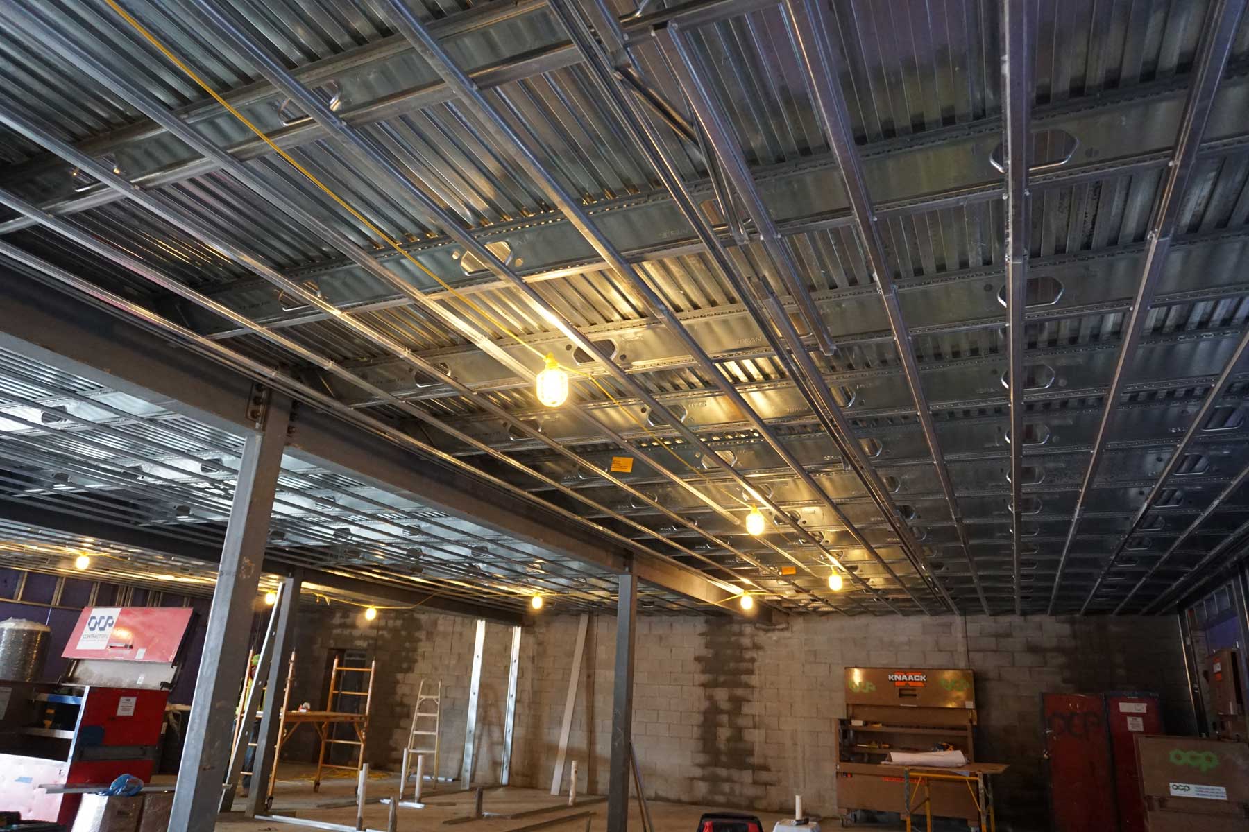 The ceiling of a building under construction with a lot of wires hanging from it.