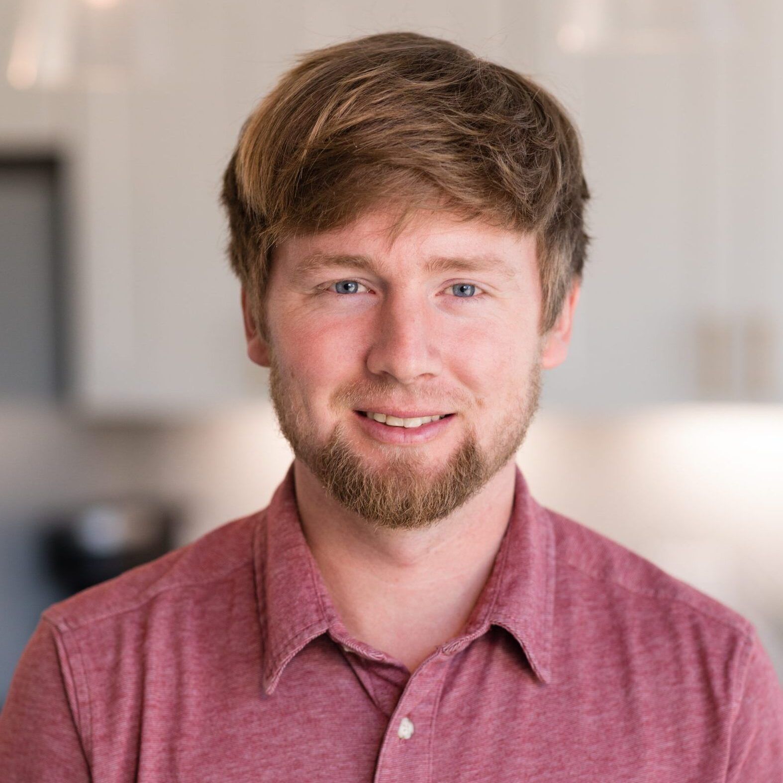 A man with a beard is wearing a red shirt and smiling. 
