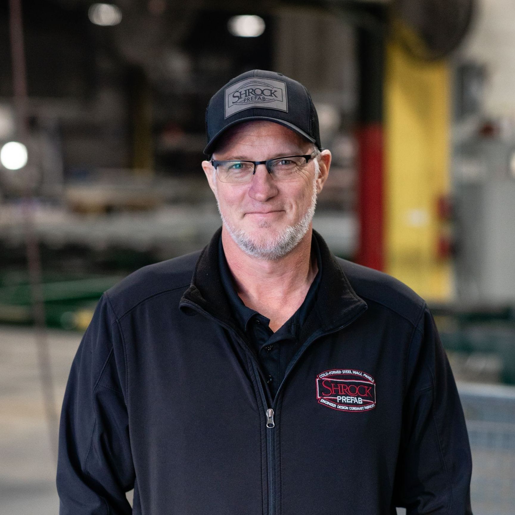 A man wearing a hat and glasses is standing in a warehouse.