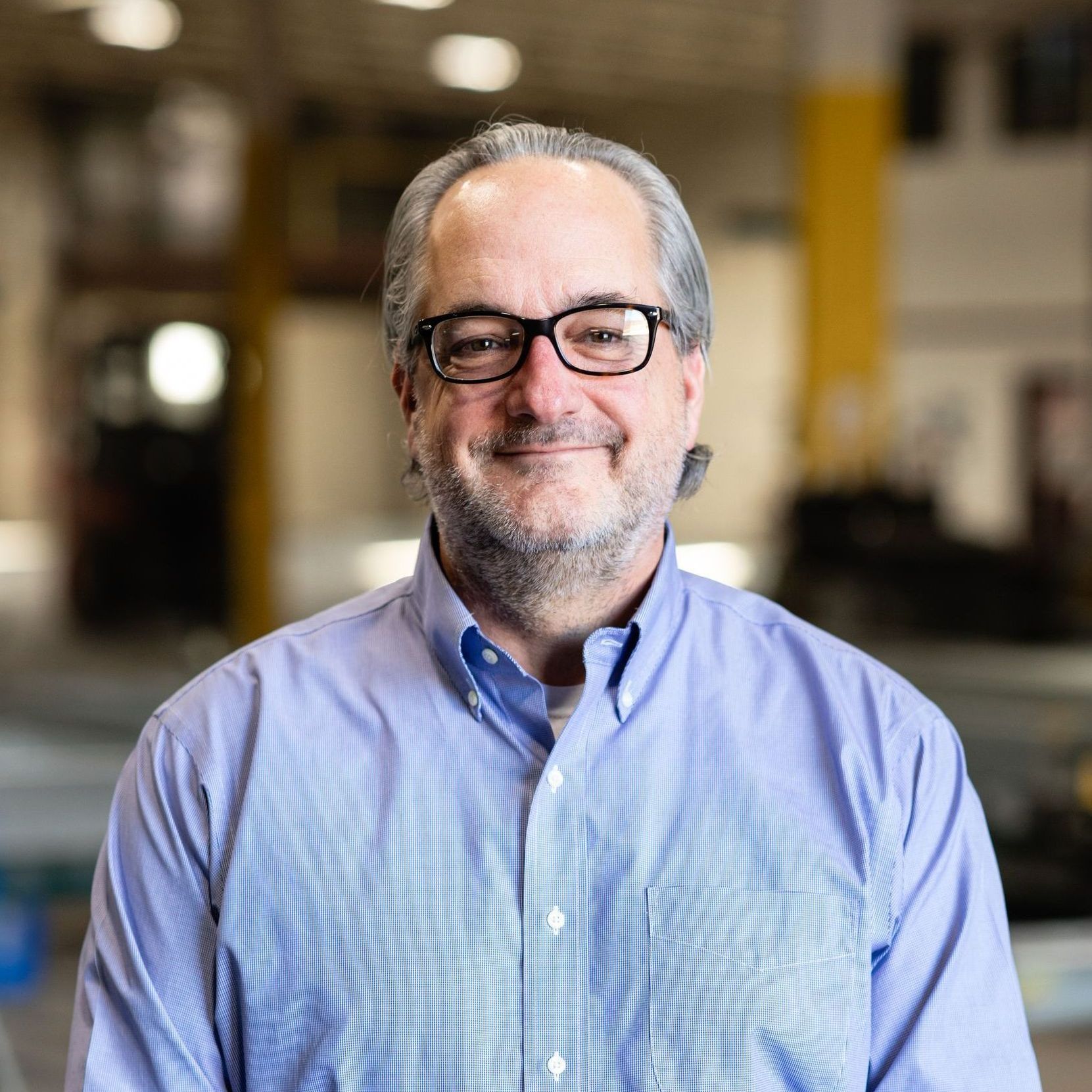 A man wearing glasses and blue shirt smiling.
