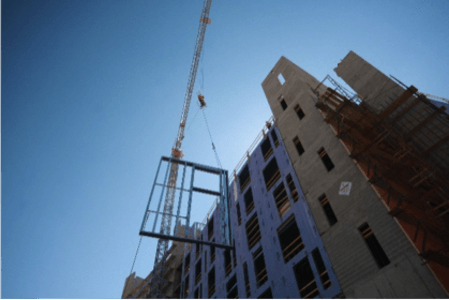 A crane is lifting a window into a building under construction.