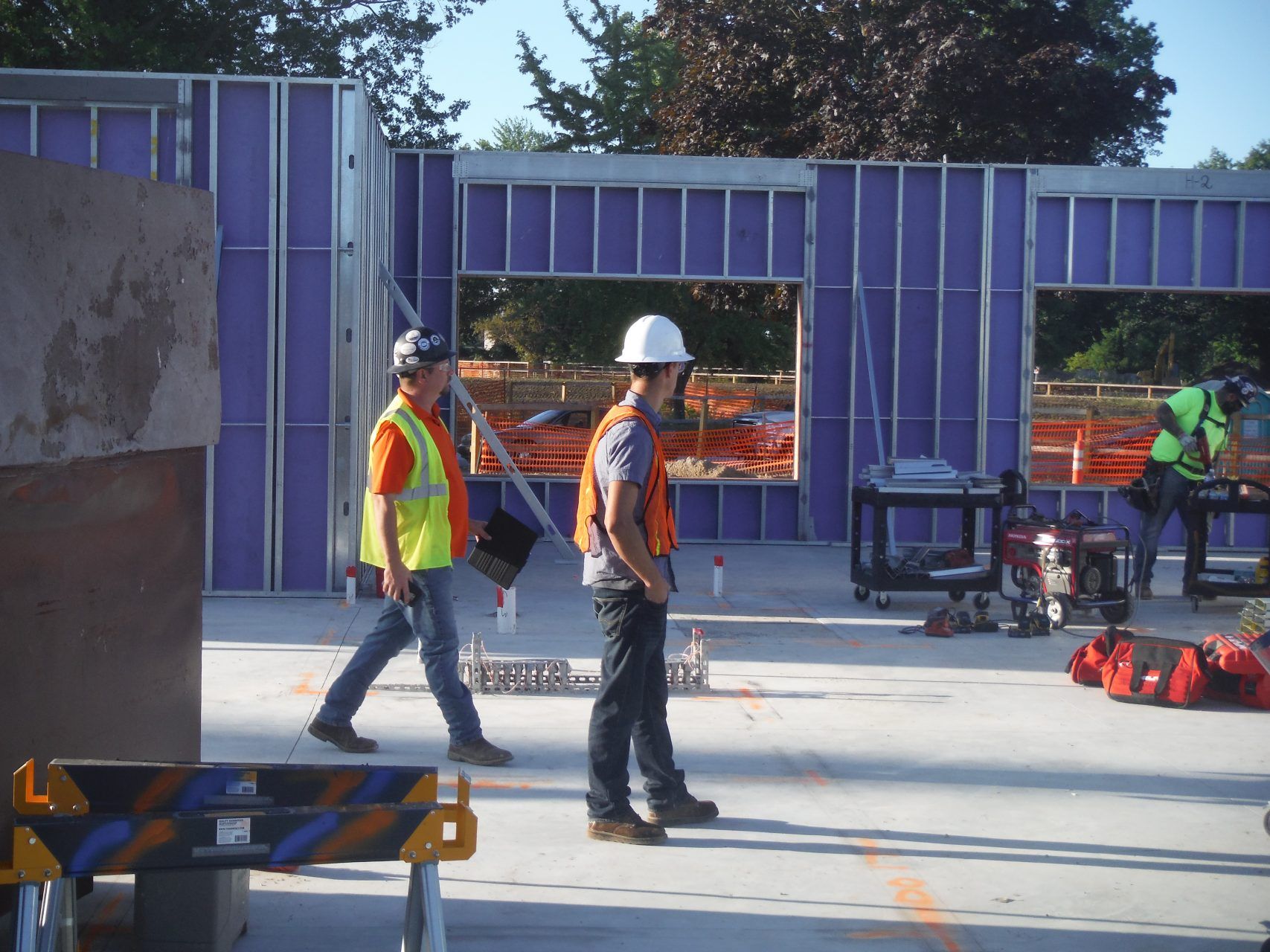 Two construction workers walking in front of a building that is under construction.