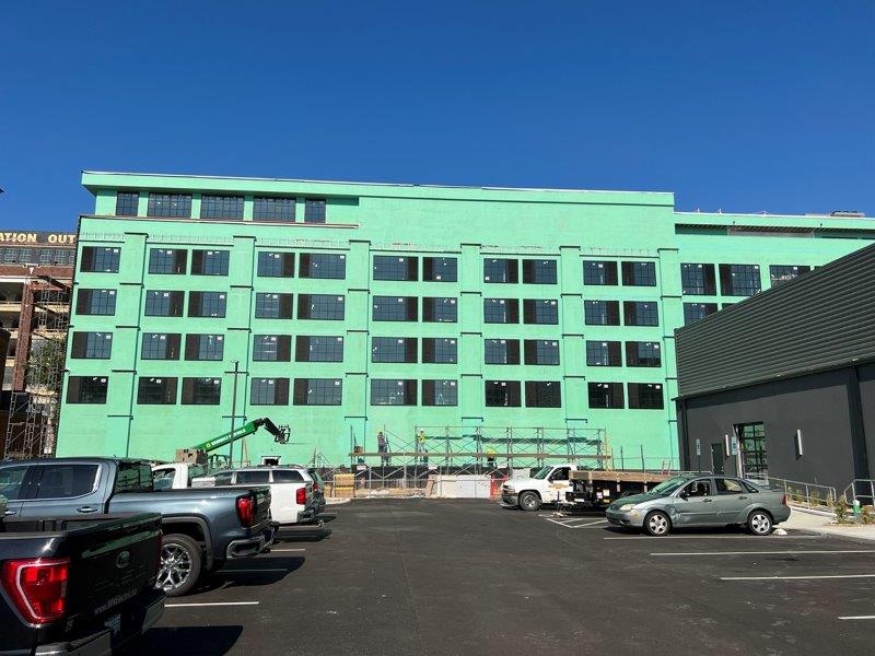 A large green building is under construction with cars parked in front of it.