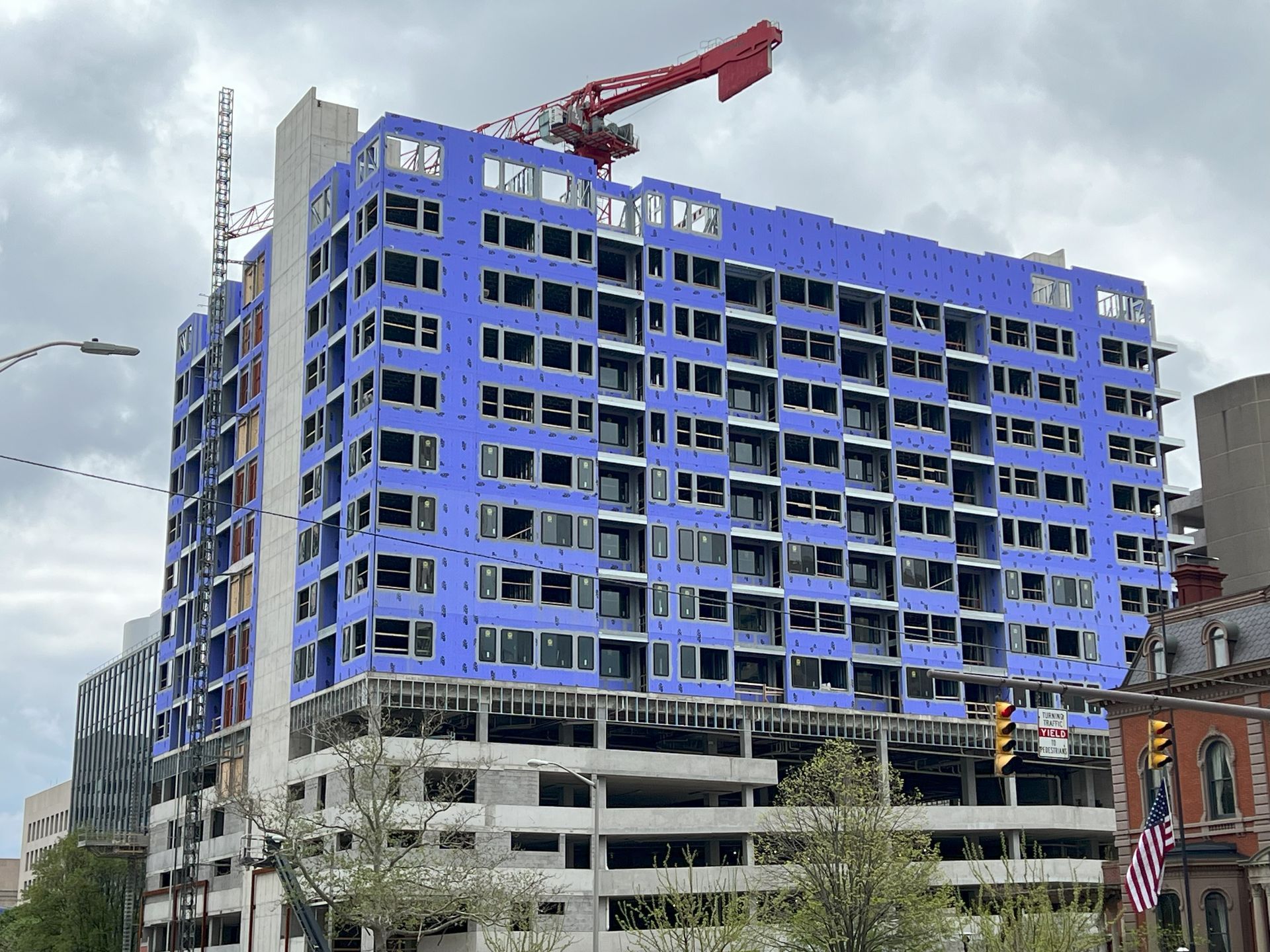 A large building with blue insulation panels is under construction in a city.