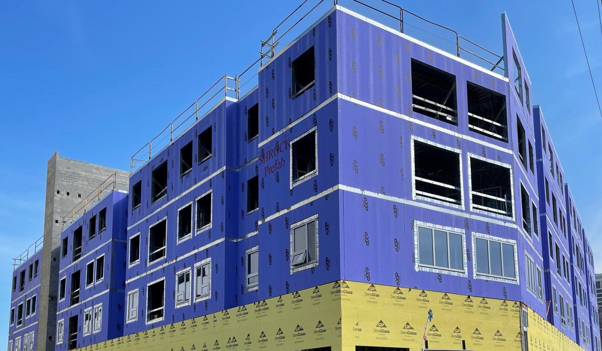 A building with purple insulation under construction with a blue sky in the background.